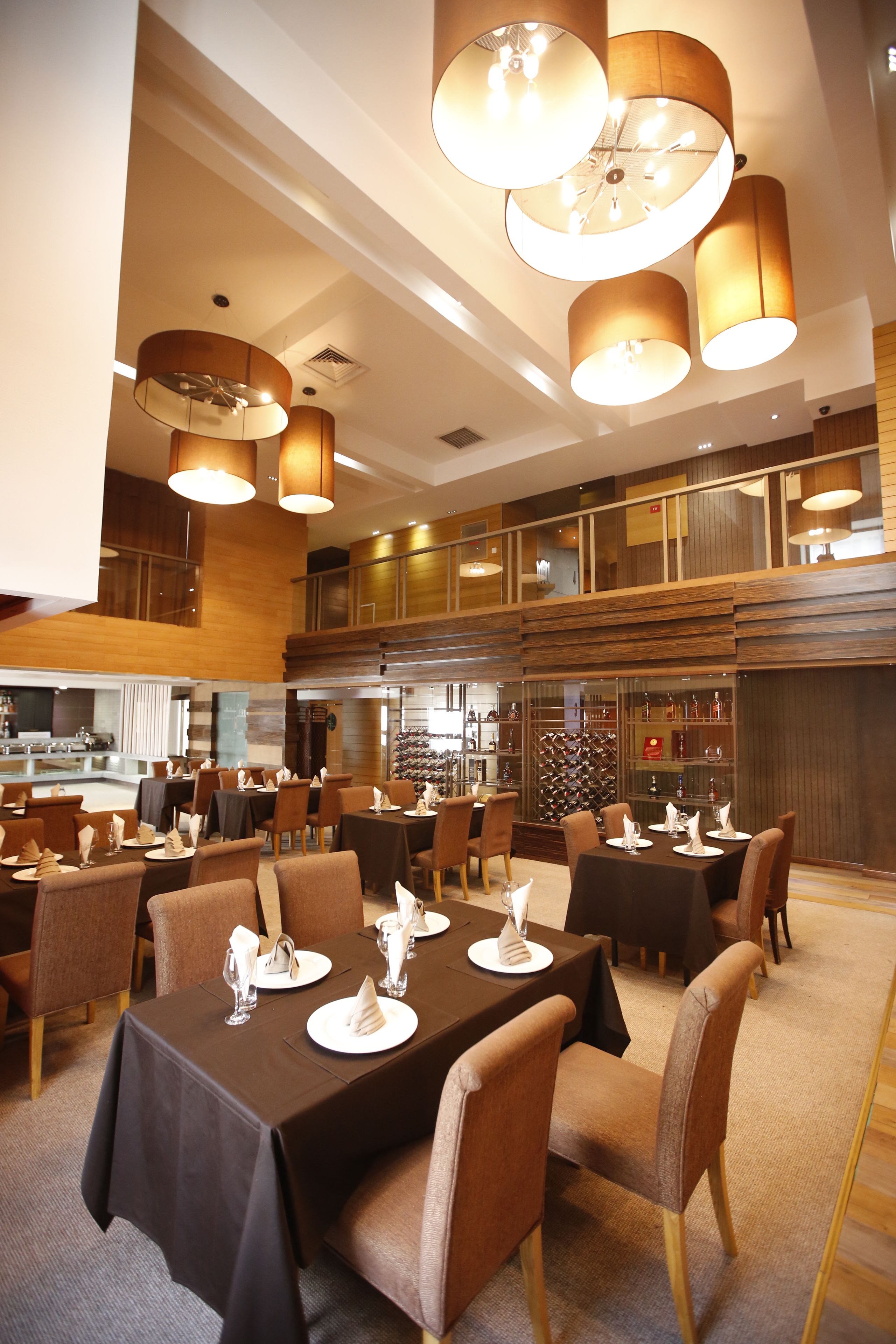Un vaste espace dédié à la salle à manger, avec plusieurs tables dressées pour les invités, agrémenté d’un lustre moderne et de panneaux de bois.