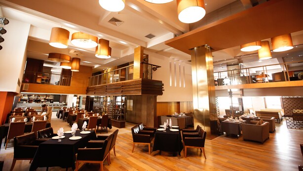 Un restaurante amplio con varias zonas de comedor, que incluyen un bar y una sala con mesas y sillas.