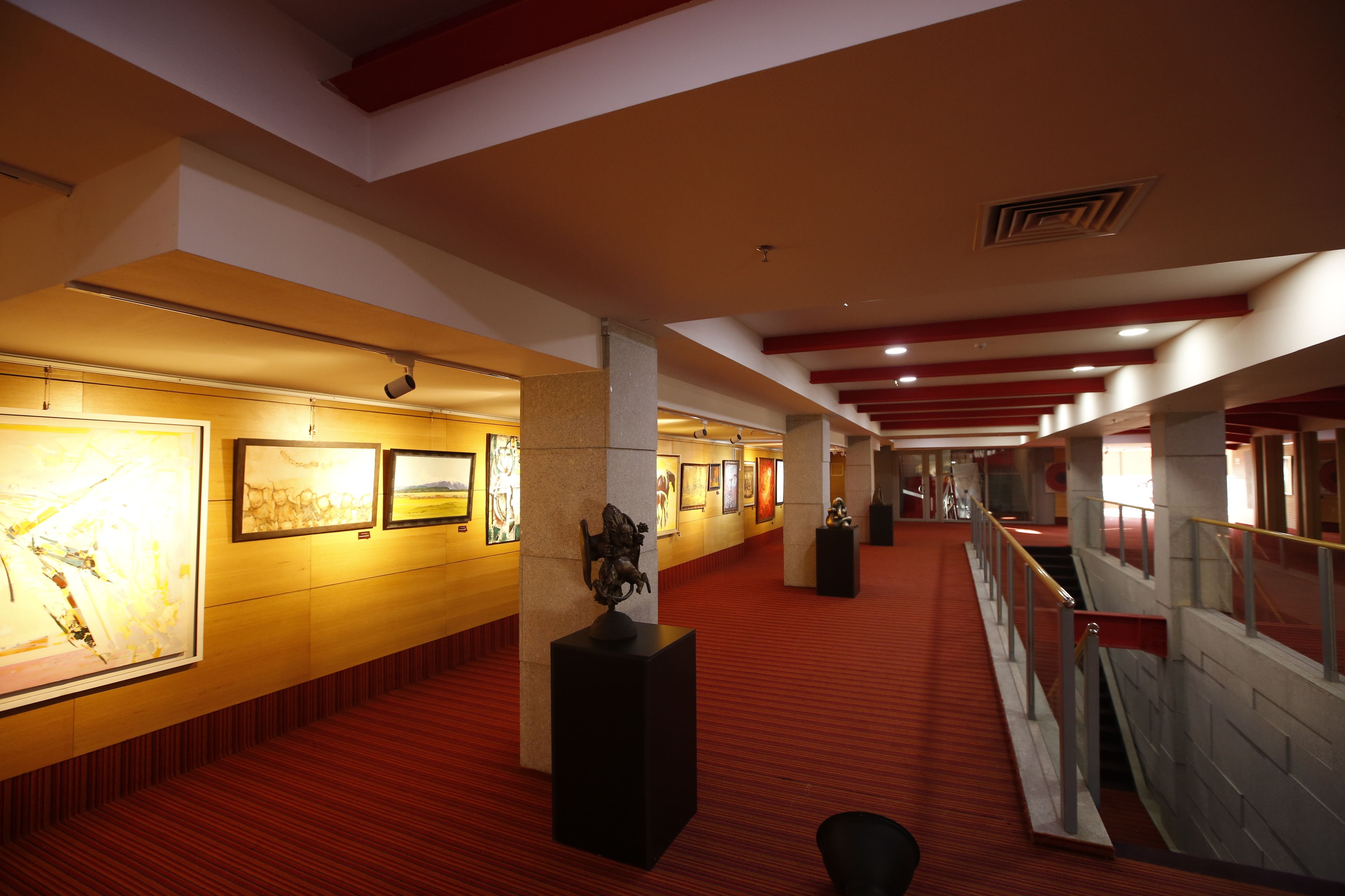 A corridor with artwork on the walls, a red carpet, and a staircase with a railing.