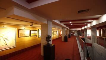 A corridor with artwork on the walls, a red carpet, and a staircase with a railing.