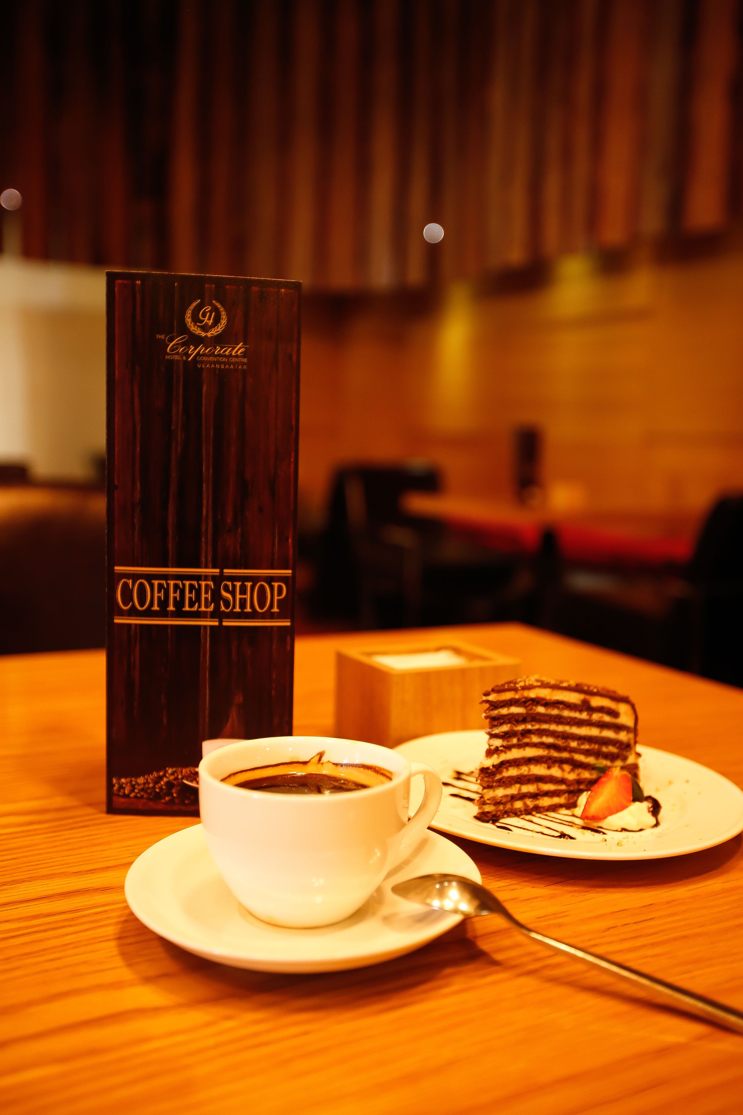 Naamplaatje van een koffiehuis, een kop koffie en een stukje taart op een tafel.