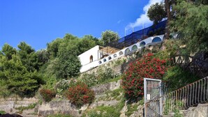 Un edificio con fachada blanca, ventanas de arco y un muro de piedra.