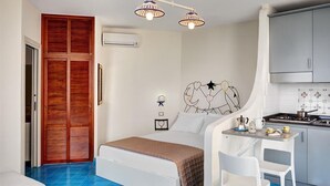 Un dormitorio con cama, mesita de noche y escritorio con silla. Cuenta con una kitchenette equipada con estufa y armarios.