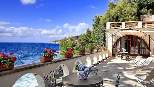 Una terraza frente al mar con mesas al aire libre, vistas al océano y plantas en macetas.