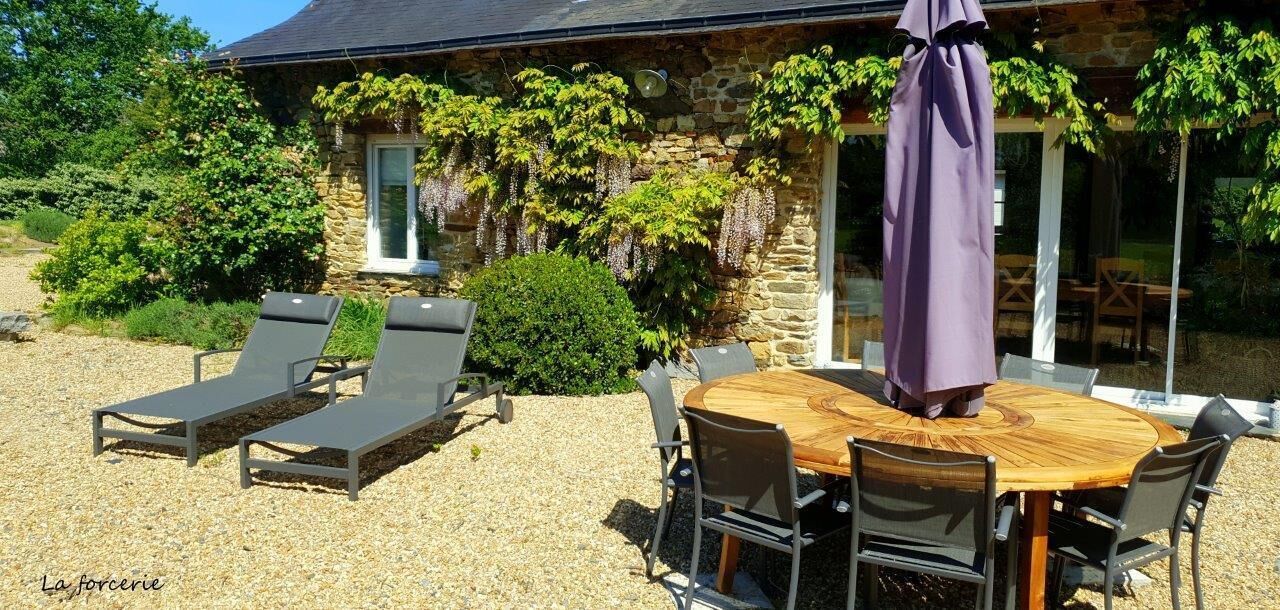 A stone house with a wooden table and chairs, a purple umbrella, and two lounge chairs.