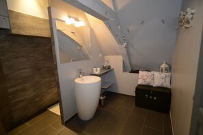 Een moderne badkamer met een groot wit wastafel, een spiegel en een klein opbergmeubeltje.