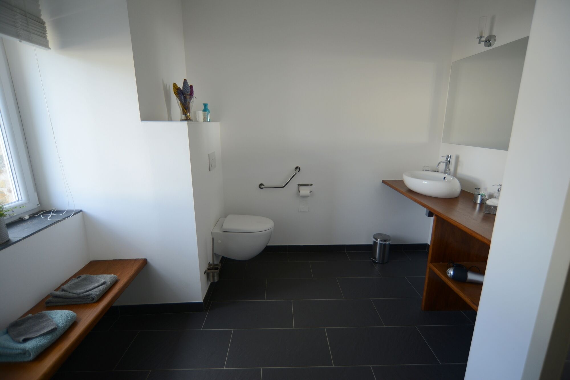 A modern bathroom with a toilet, sink, and a bench with towels.