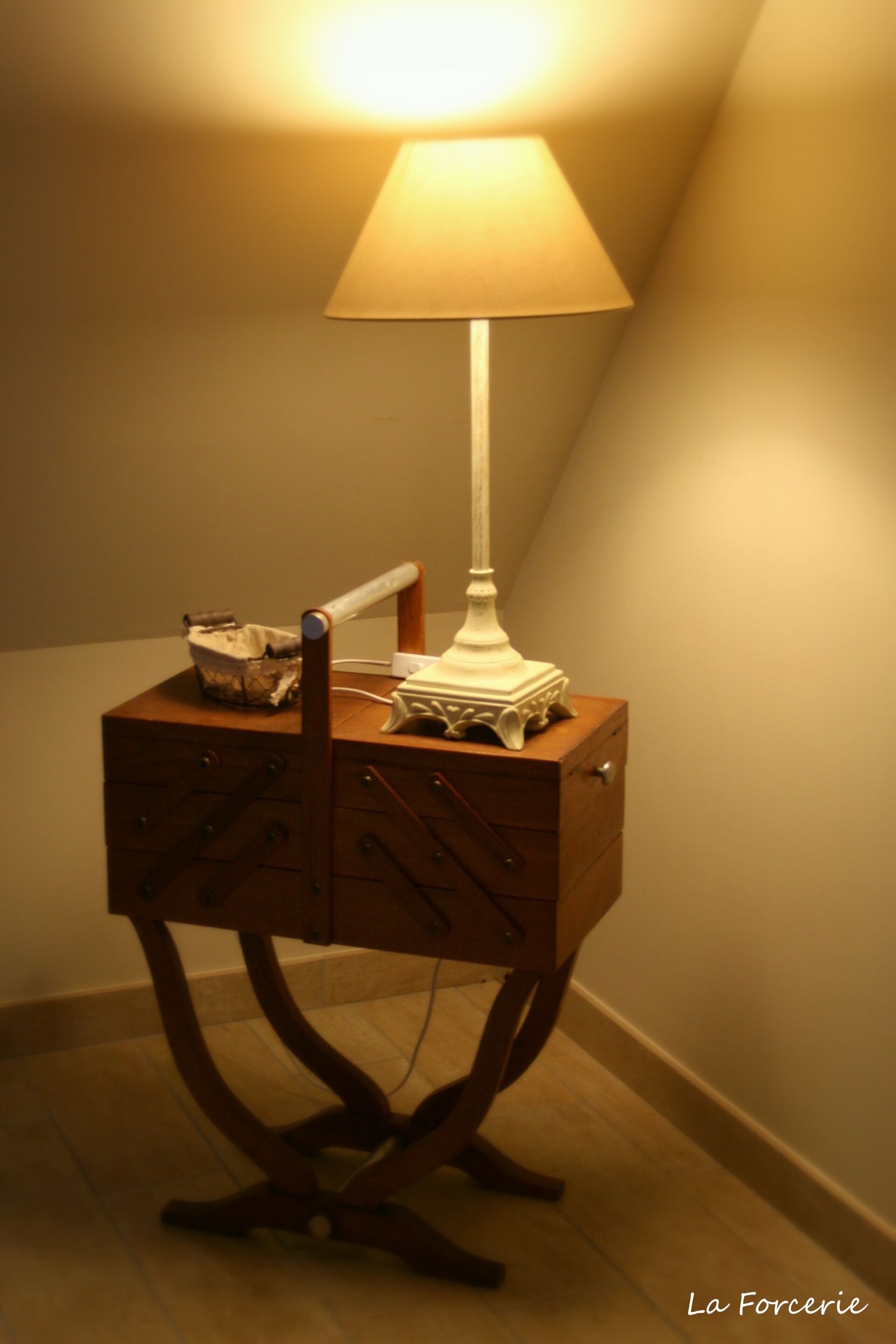 A wooden bedside table with a white lamp, a basket, and a small electronic device.