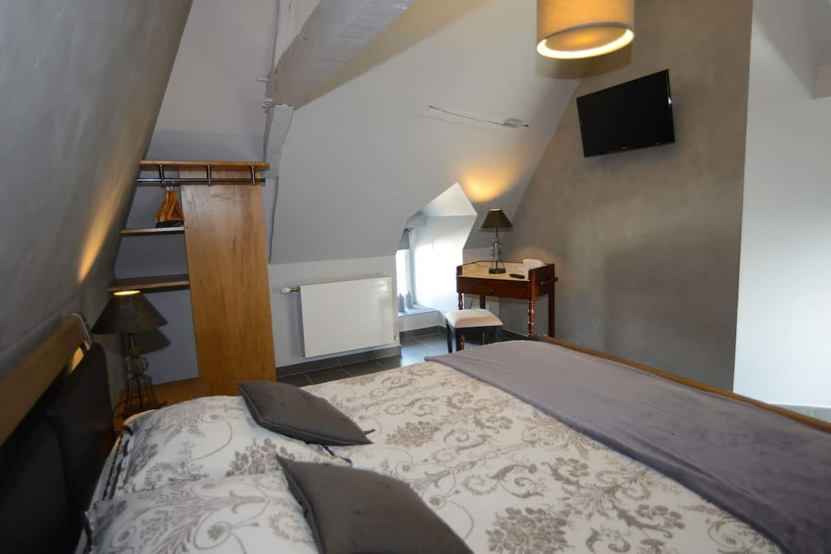 Une chambre à coucher comprenant un lit, un bureau, une chaise, une lampe et un téléviseur fixé au mur.