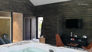 Een modern interieur met een bubbelbad, een aan de muur bevestigde televisie en een schuifdeur naar een buitenruimte.