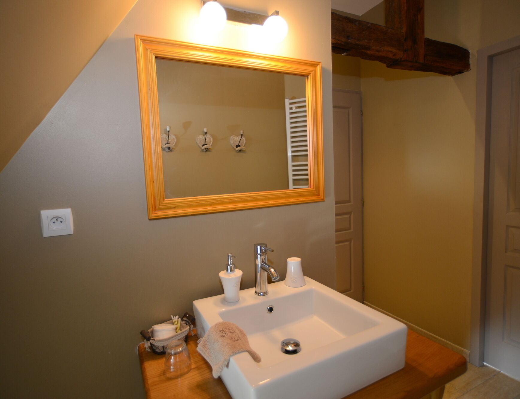 A bathroom with a white sink, a mirror with a wooden frame, and a towel rack with three towels.