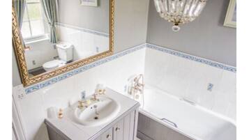 A bathroom with a large mirror, a sink, a bathtub, and a chandelier.