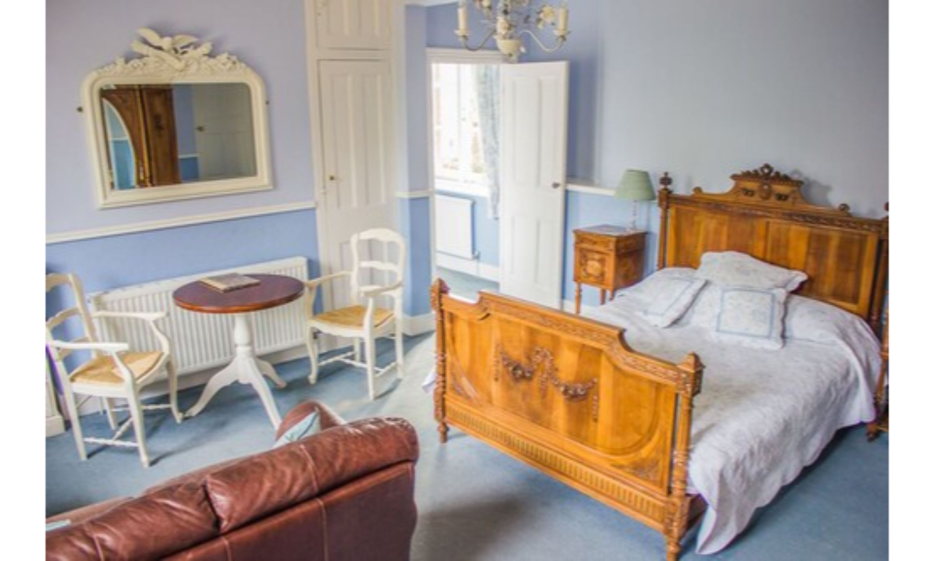A bedroom with a wooden bed, a round table with chairs, a radiator, and a mirror on the wall.