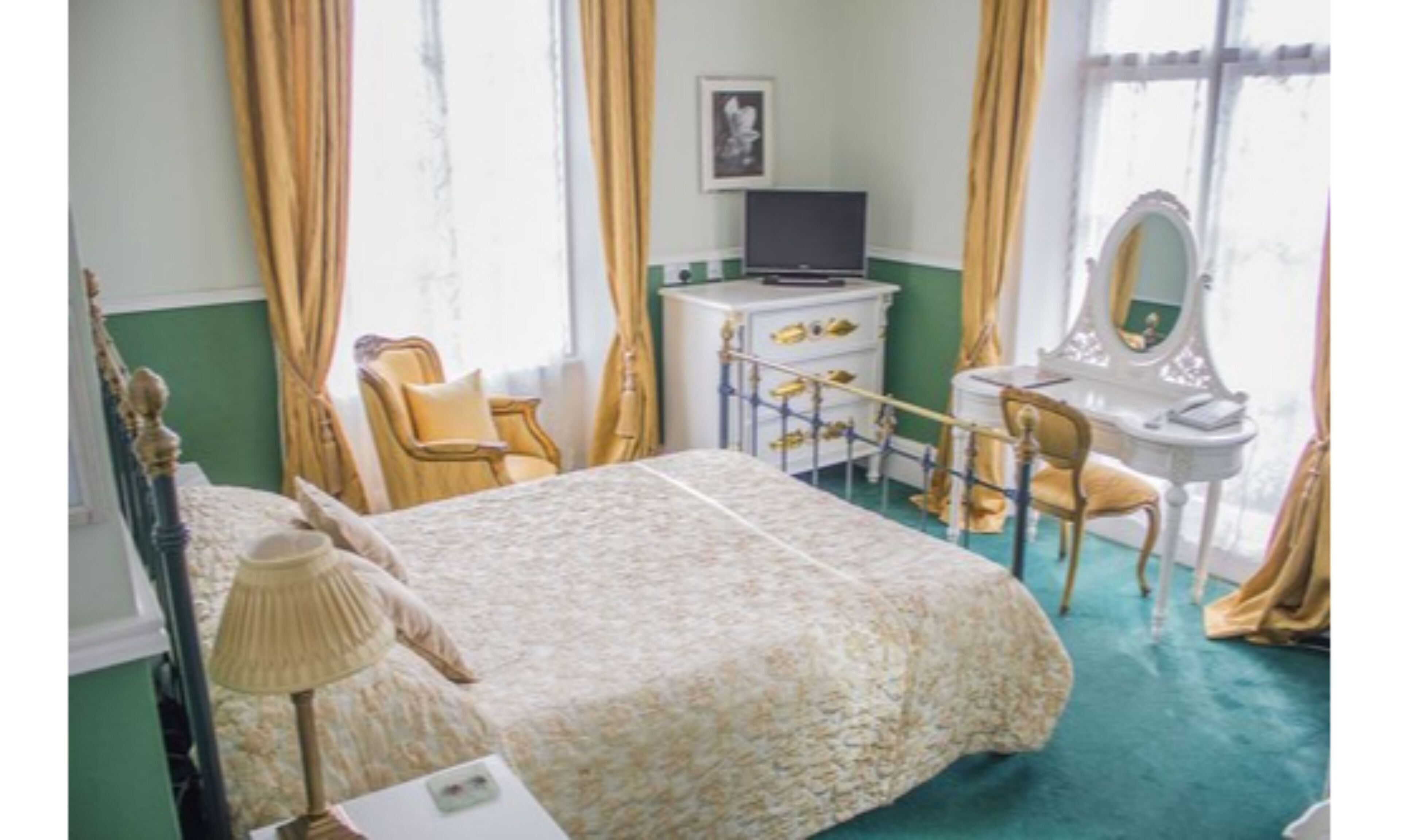 Een slaapkamer met een bed, een bureau, een stoel, een lamp en een dressoir.