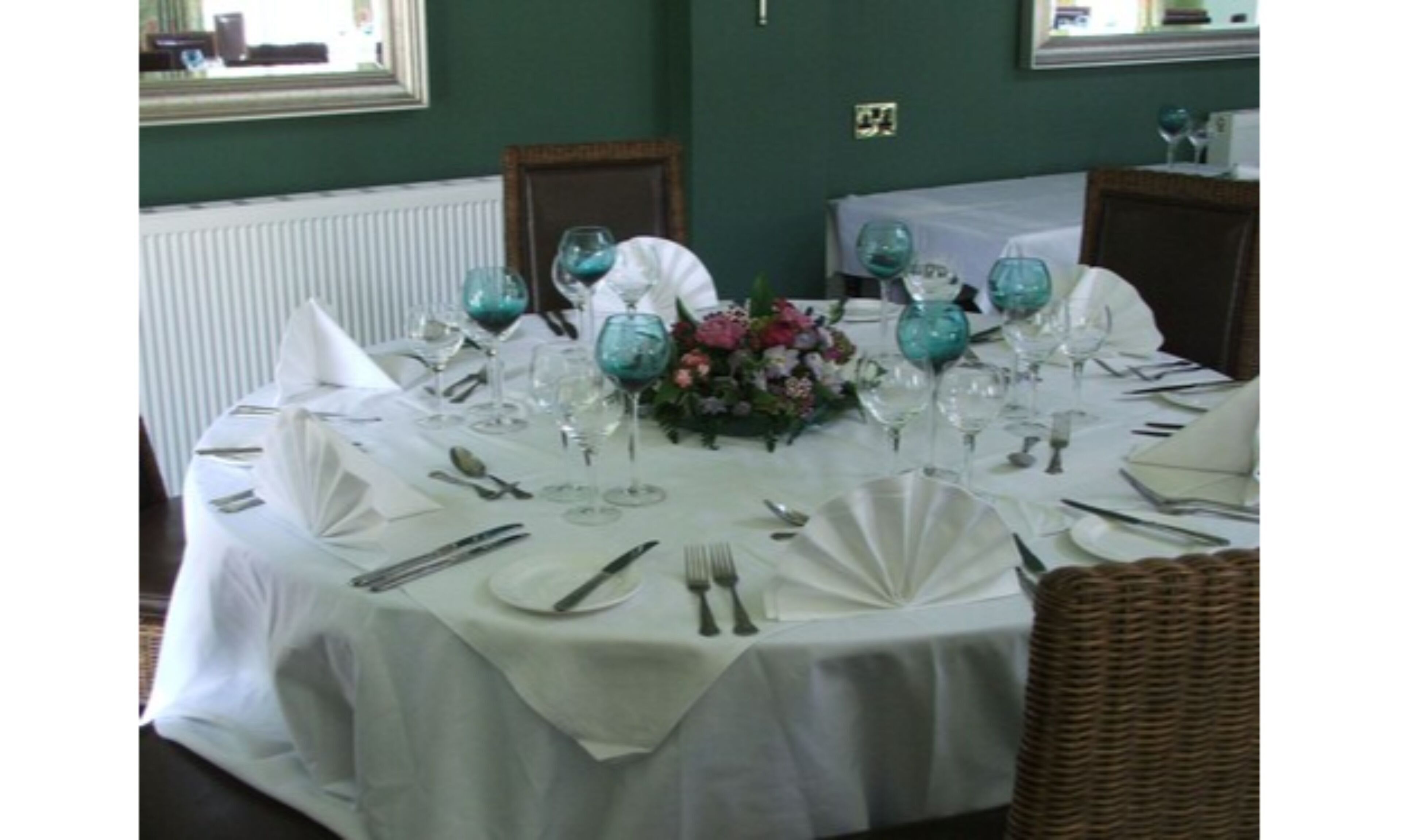 A dining table set for a formal meal with white tablecloths, glassware, and a floral centerpiece.