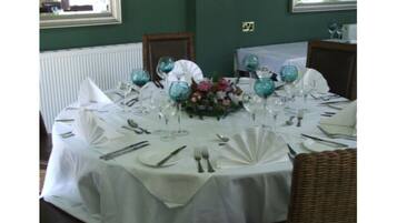A dining table set for a formal meal with white tablecloths, glassware, and a floral centerpiece.
