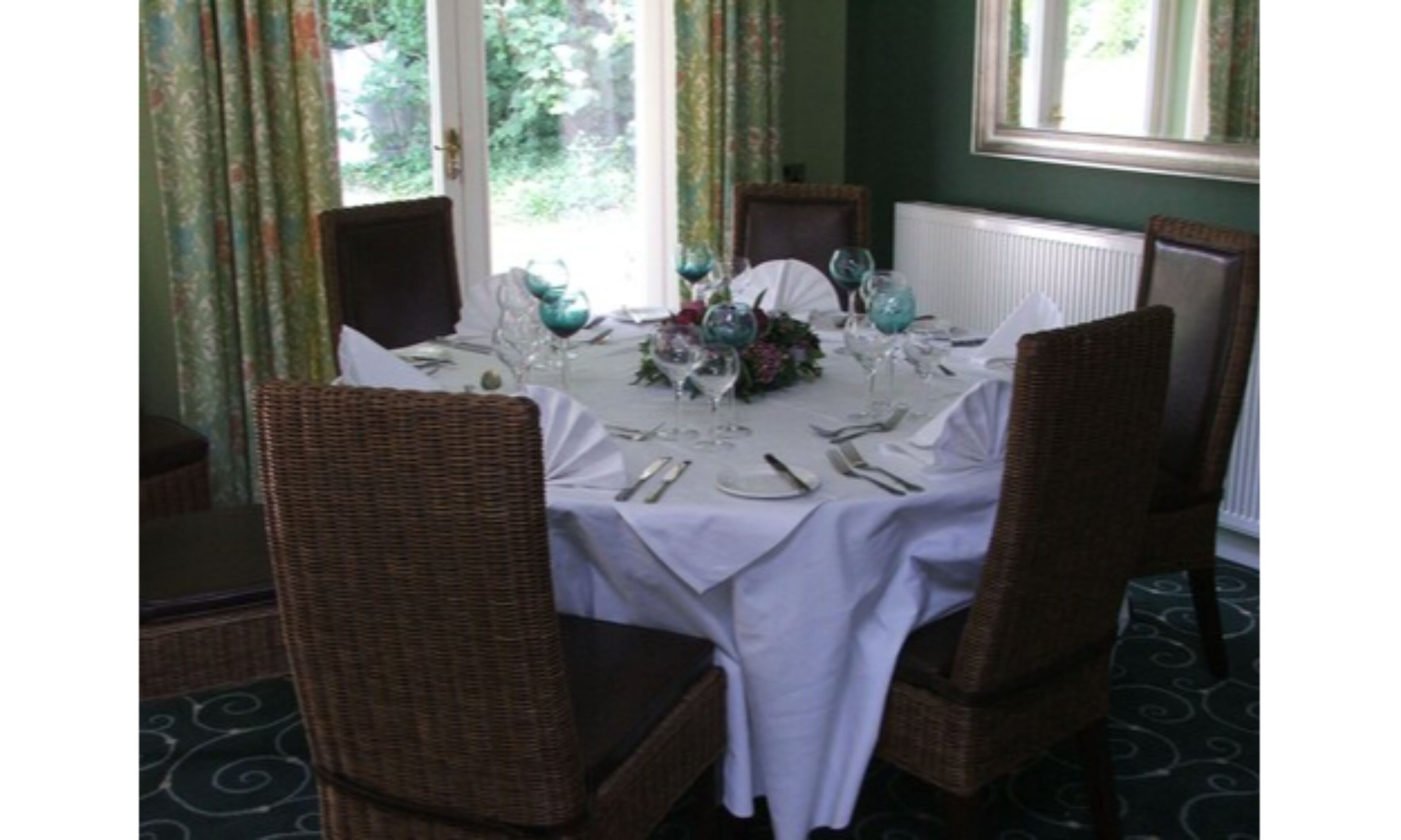 A dining table set for four with wicker chairs, a white tablecloth, and a floral centerpiece.