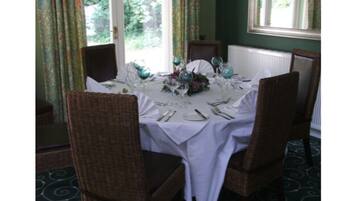 A dining table set for four with wicker chairs, a white tablecloth, and a floral centerpiece.