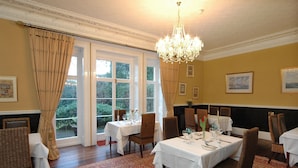 A dining room with tables set for a meal, large windows, and a chandelier. - Albert Cottage Hotel (East Cowes)