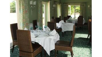 A dining area with tables set for two, wicker chairs, and a patterned carpet.