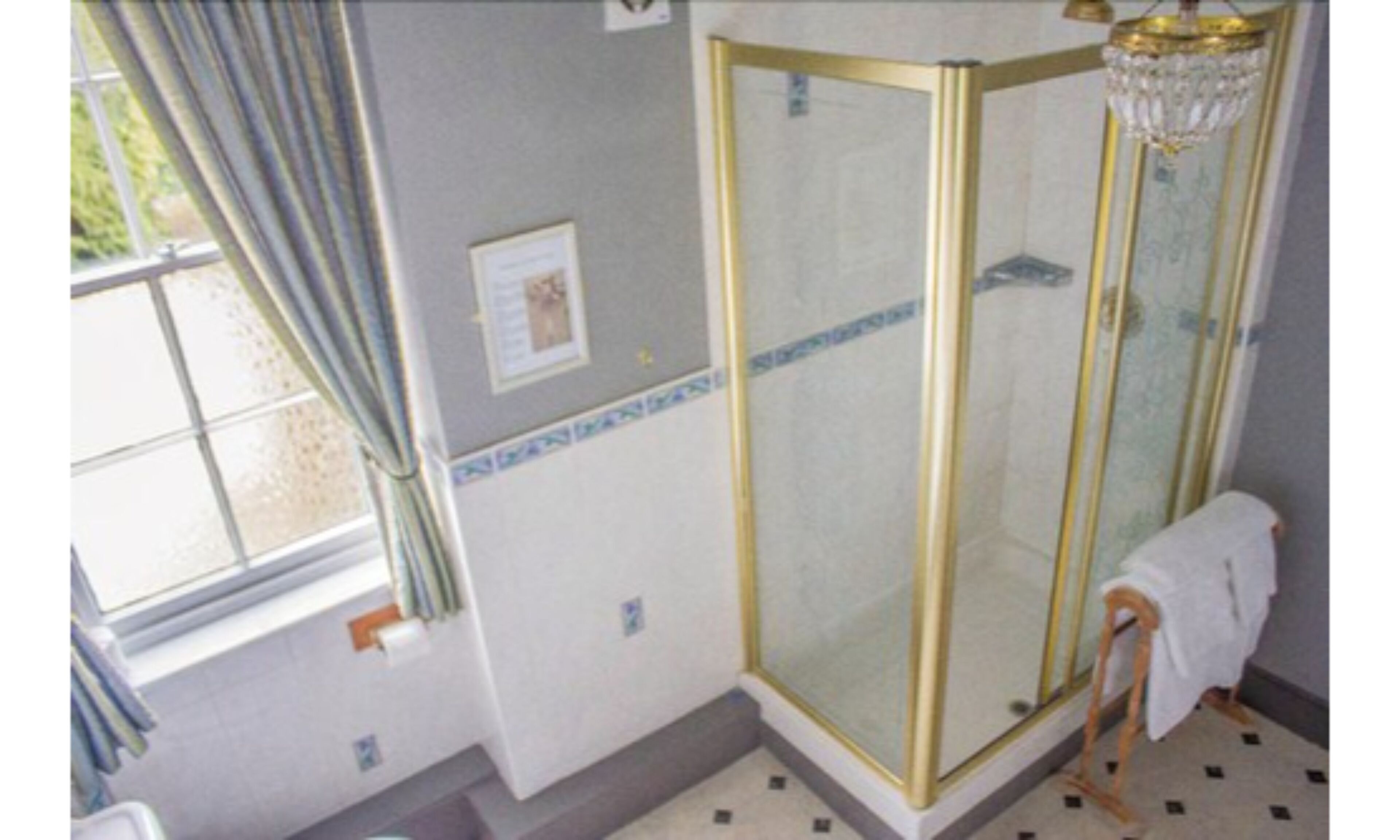 A bathroom with a glass shower enclosure, a window with curtains, and a chandelier.