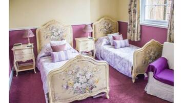 A bedroom with two beds, a nightstand, a chair, and a window with curtains.