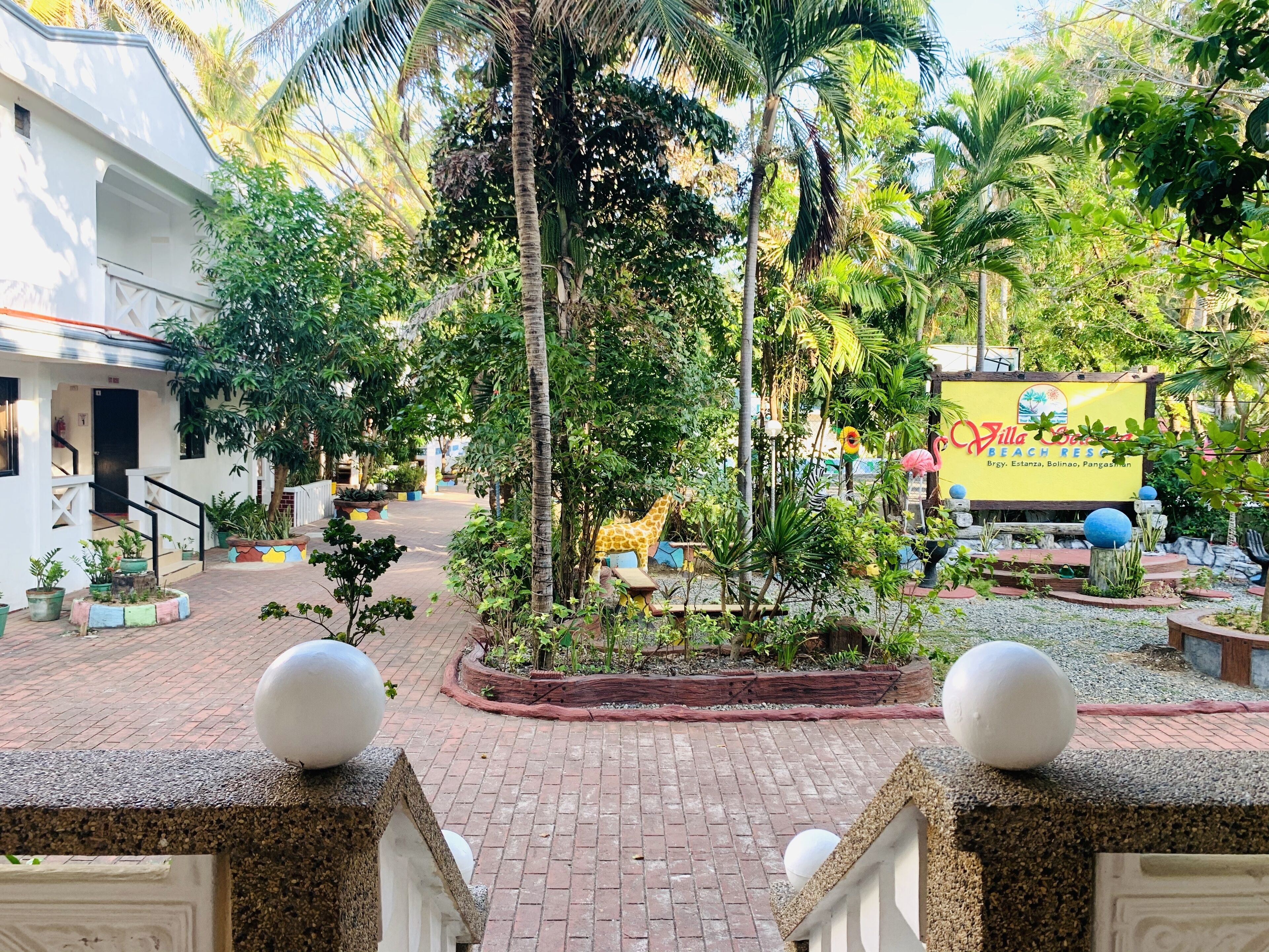 A courtyard with a palm tree, a giraffe statue, and a sign for Villa Serene Beach Resort.
