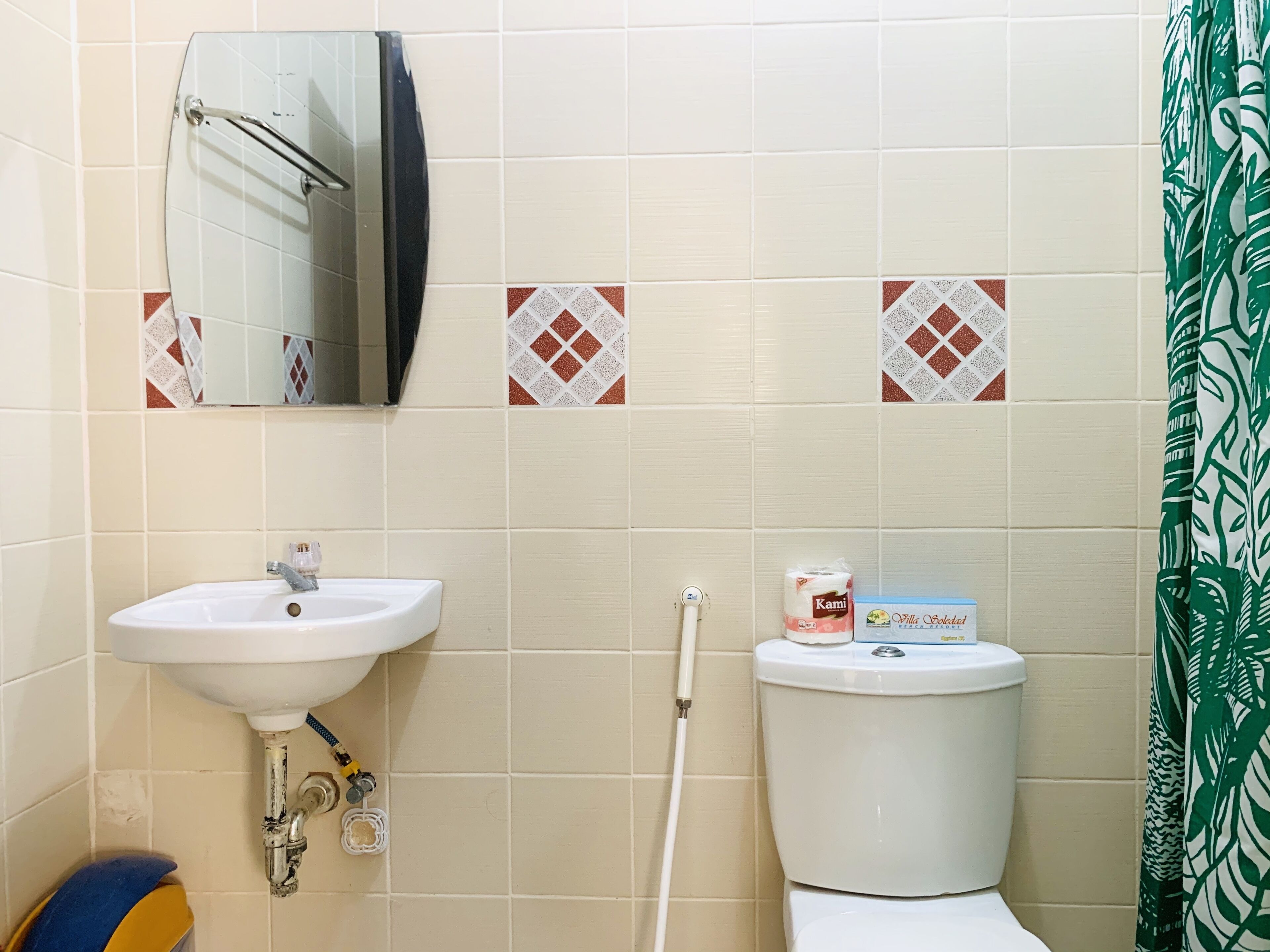 A bathroom with a white sink, a toilet, and a mirror. There are patterned tiles on the wall and a green curtain.