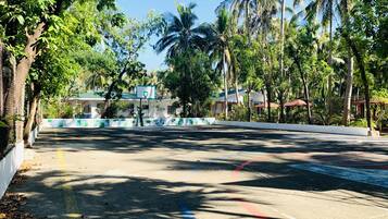 A paved road with a basketball court, surrounded by trees and buildings.