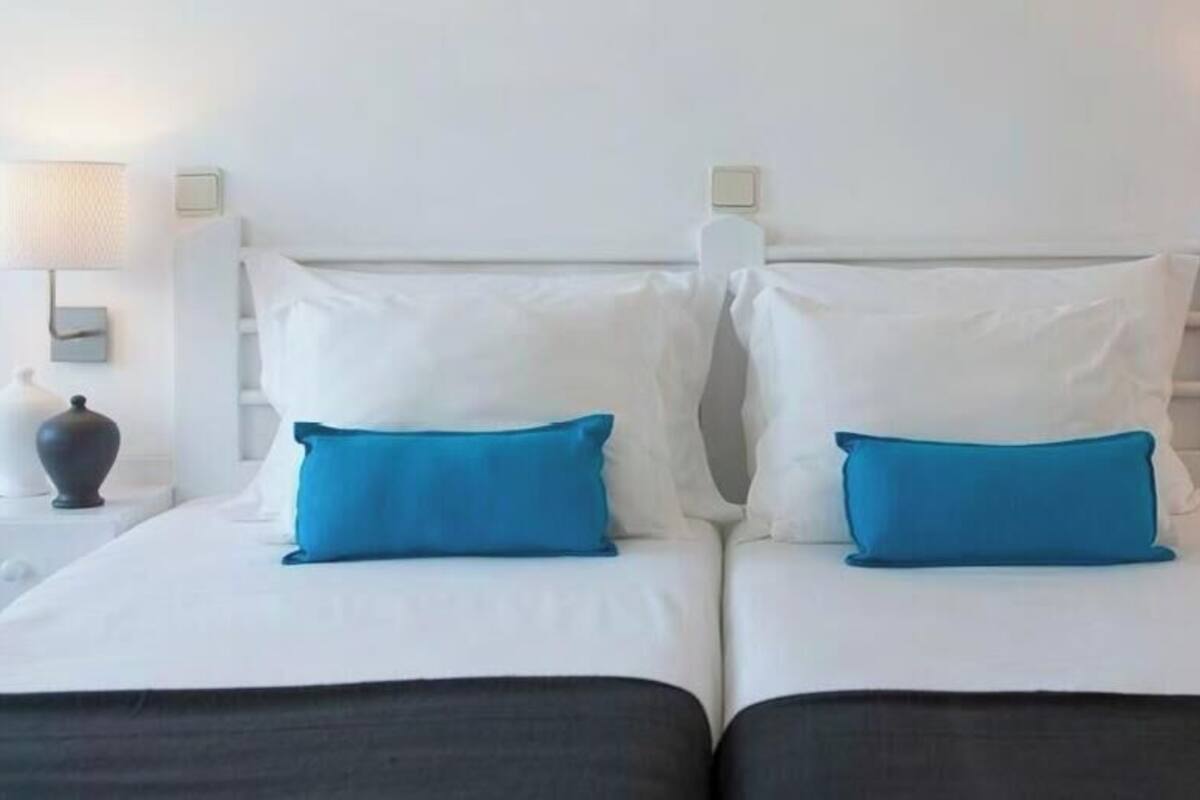 A double bed with white and blue bedding, two bedside tables with lamps, and a white wall.