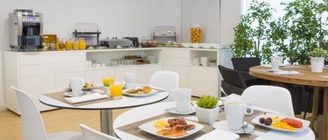 A modern breakfast area with white furniture, a coffee machine, and a variety of breakfast items on the counter.