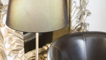 A lamp with a textured shade, a leather armchair, and a decorative mirror with a floral pattern.