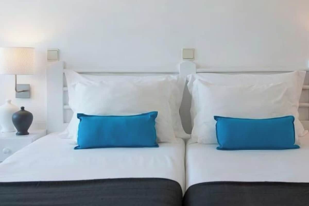A double bed with white and blue bedding, two bedside tables with lamps, and a white wall.