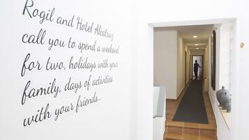 A hallway with a person walking away, a black carpet, and a tiled floor.