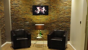 A room with a stone wall, two leather armchairs, a TV, and a lamp. - Hotel Rheinischer Hof (Erkelenz)