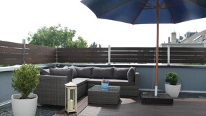 A rooftop patio with a sectional sofa, a small table, and potted plants. - Hotel Rheinischer Hof (Erkelenz)