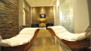 A spa area with two massage tables, a stone wall, a television, and a mirror. - Hotel Rheinischer Hof (Erkelenz)