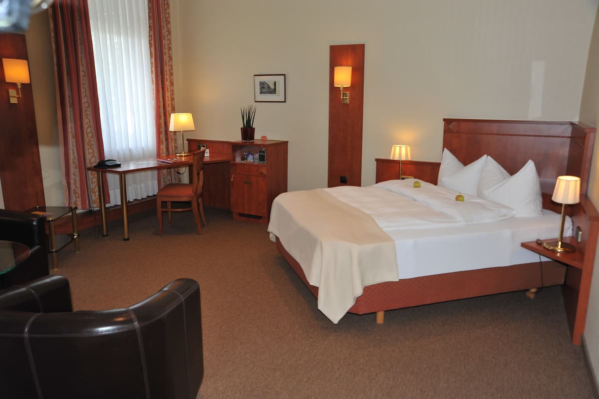 Quarto de hotel com cama, escrivaninha, cadeira e duas luminárias de apoio.