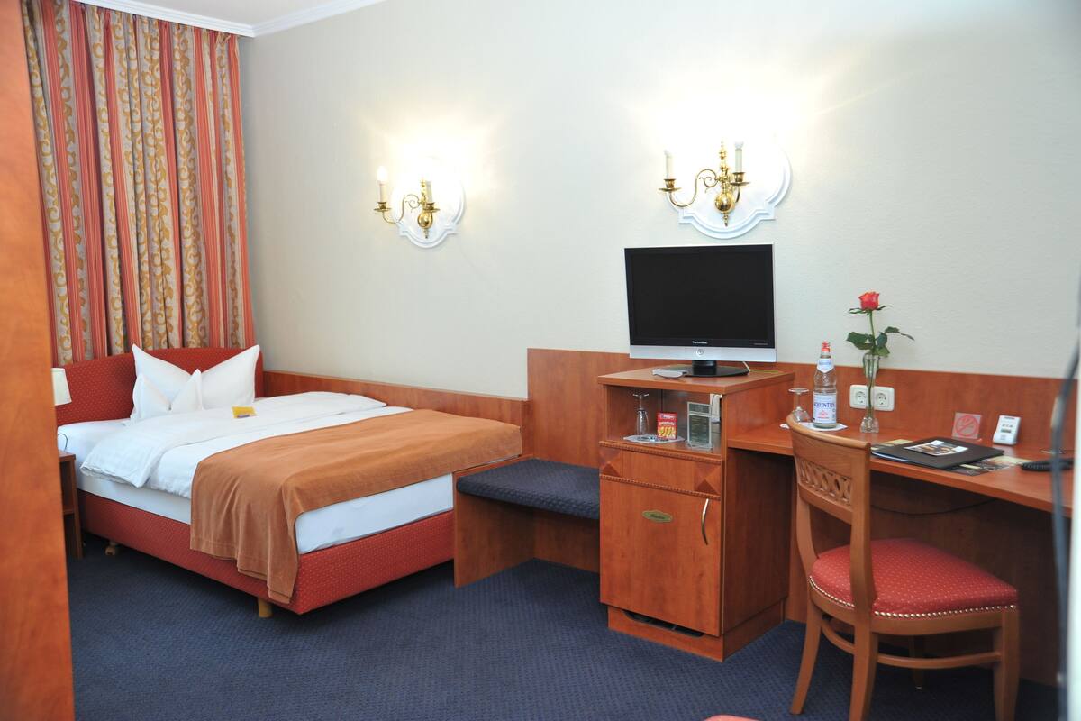 Quarto de hotel com uma cama, uma mesa, uma cadeira, uma televisão e um pequeno armário.