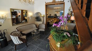 A spacious living room with a chandelier, striped sofa, armchairs, and a coffee table. There is a mirror on the wall and a potted plant with purple flowers. - Hotel Rheinischer Hof (Erkelenz)