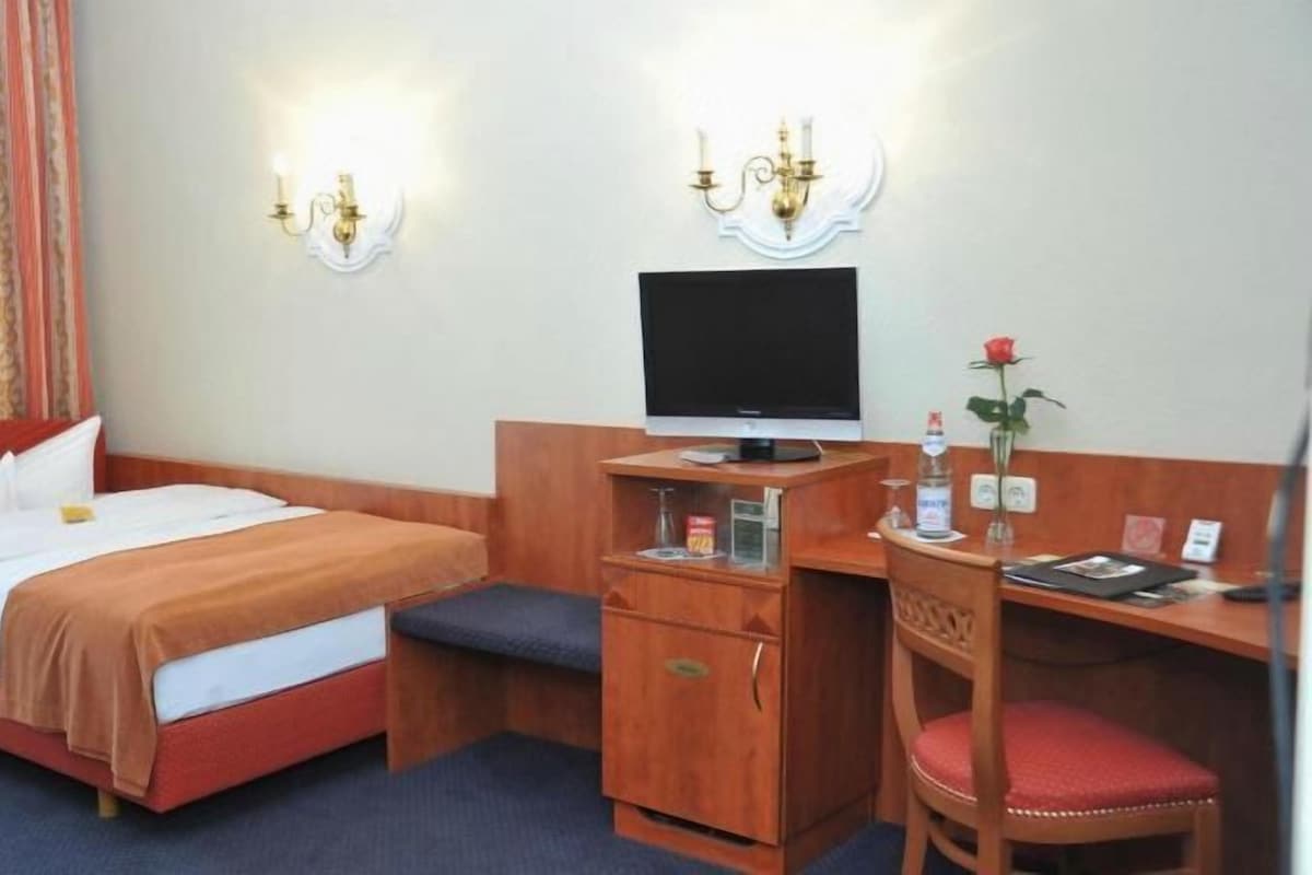 A hotel room with a bed, a desk, a chair, a television, and a small cabinet.