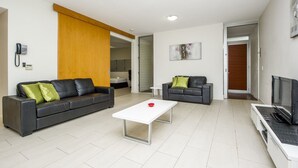 Un salon moderne avec deux canapés en cuir foncé, une table basse blanche, un téléviseur à écran plat et une porte coulissante en bois.