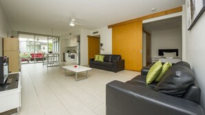 Un salon moderne avec un canapé en cuir noir, une table basse blanche et un coin repas comprenant une table et des chaises rouges.
