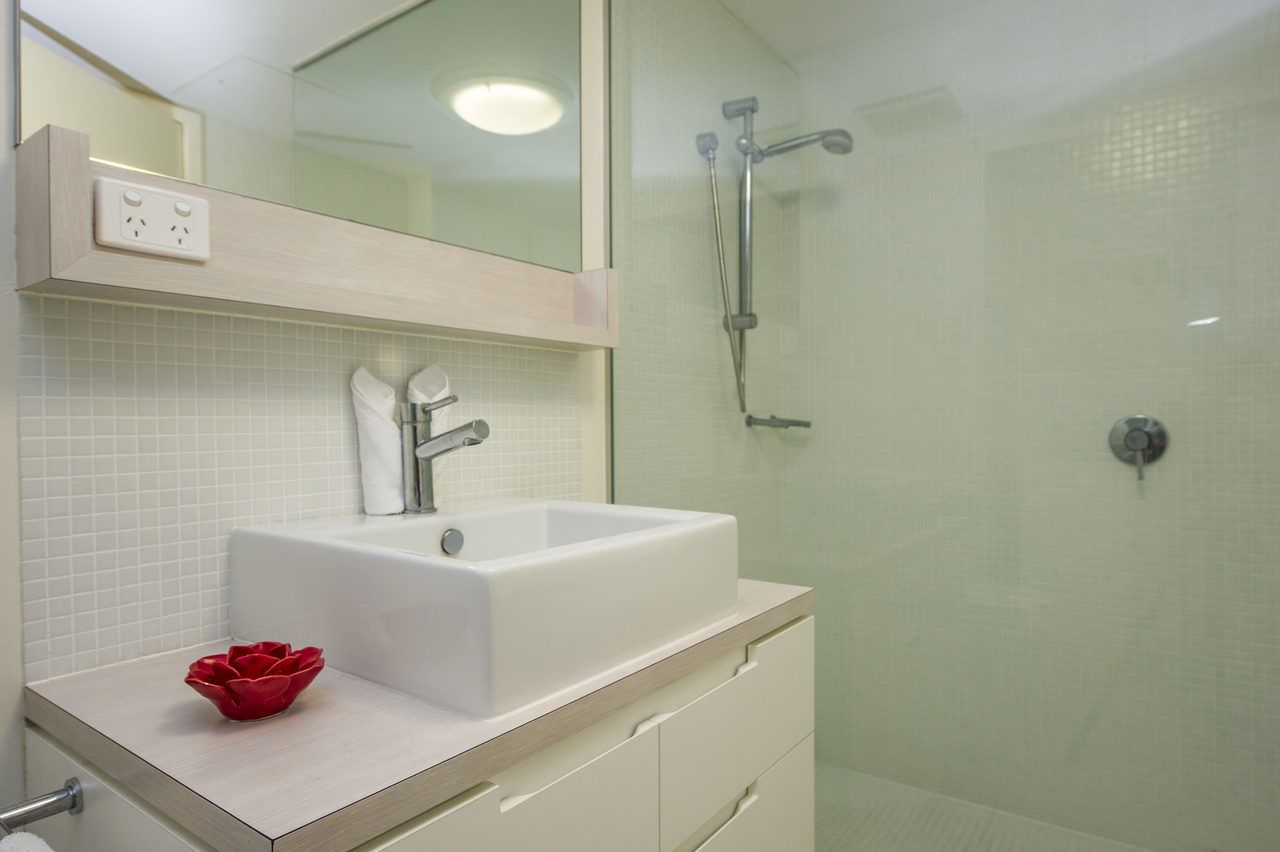 A modern bathroom with a white sink, a glass shower enclosure, and a mirror above the sink.