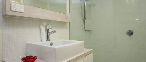 A modern bathroom with a white sink, a glass shower enclosure, and a mirror above the sink.