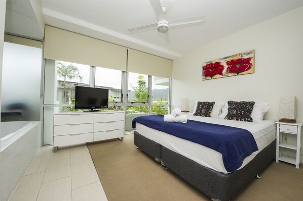 A modern bedroom with a bed, a television, a ceiling fan, and a large window with a view of greenery. - 1 Bright Point Apartment 1208 (Nelly Bay)