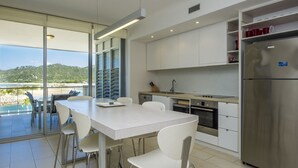A modern kitchen with white cabinets, a stainless steel refrigerator, and a dining area with a table and chairs. - 1 Bright Point Apartment 1401 (Nelly Bay)