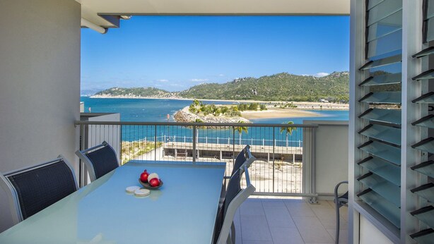 A balcony with a table and chairs, overlooking a beach and ocean. - 1 Bright Point Apartment 1401 (Nelly Bay)