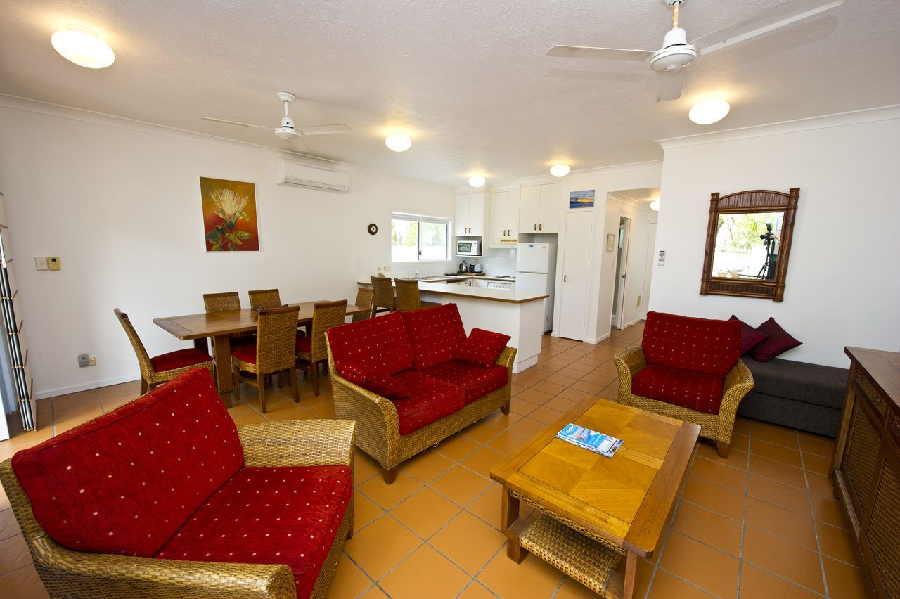 Ampla sala de estar com móveis de vime, uma mesa de jantar e um espaço de cozinha ao fundo.