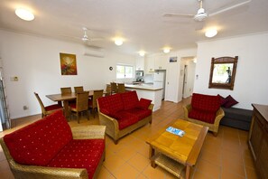 A spacious living area with wicker furniture, a dining table, and a kitchenette in the background. - Beachcomber Unit 2 (Arcadia)